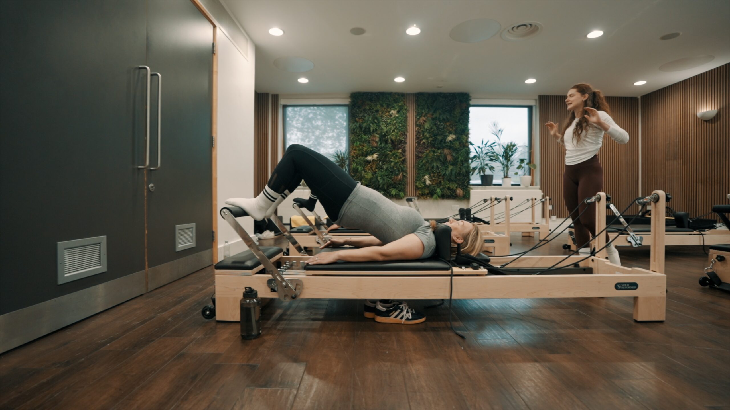 A woman on a reformer with her knees raised while the instructor leads the class